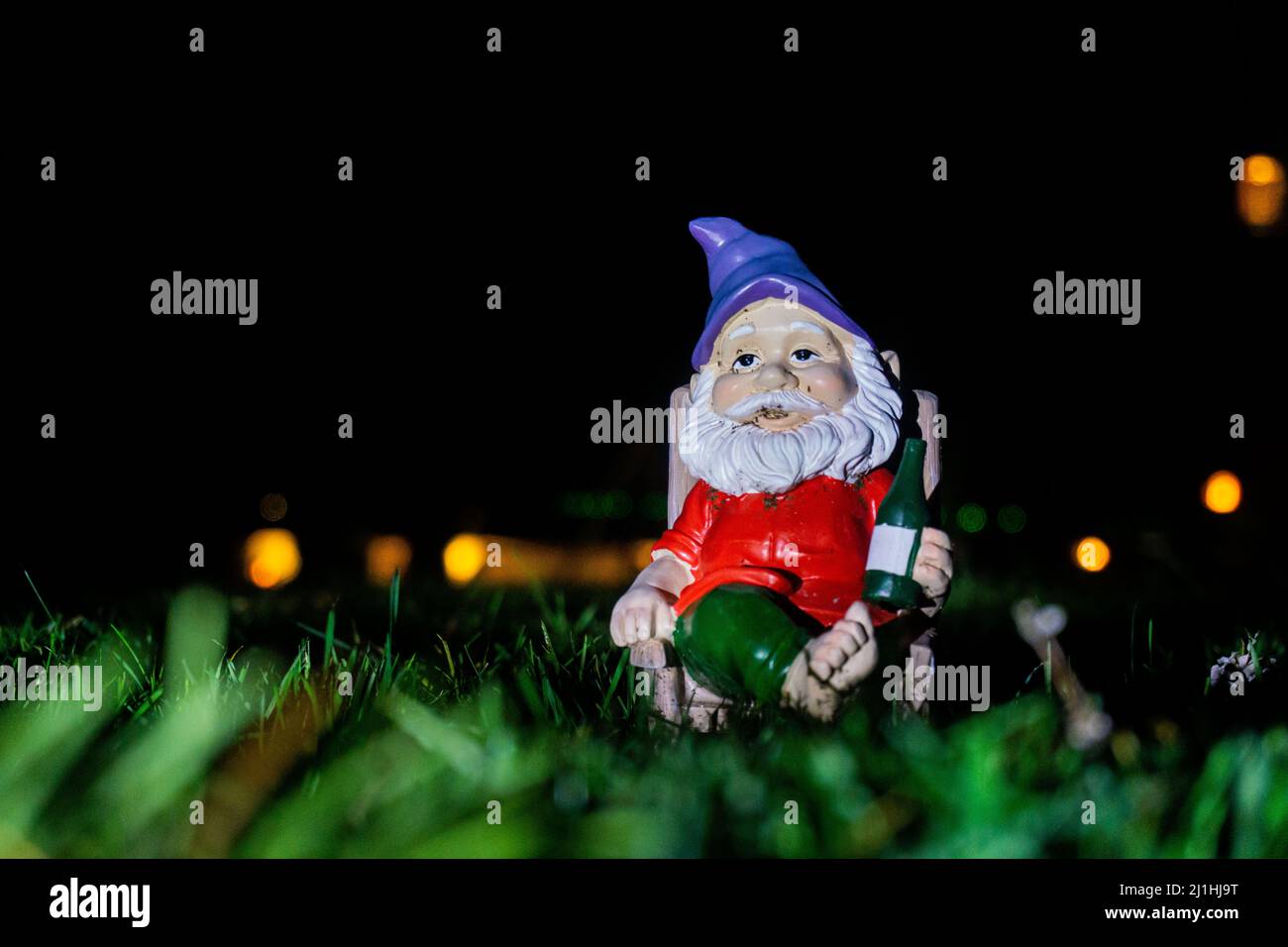 Garden gnome in front of black background relaxing on top of green grass in the middle of the night. Stock Photo
