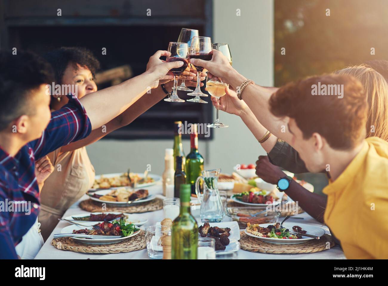Sharing a toast with the best company in the world. Shot of a group of friends raising up their glasses for a toast while sitting around a table Stock Photo