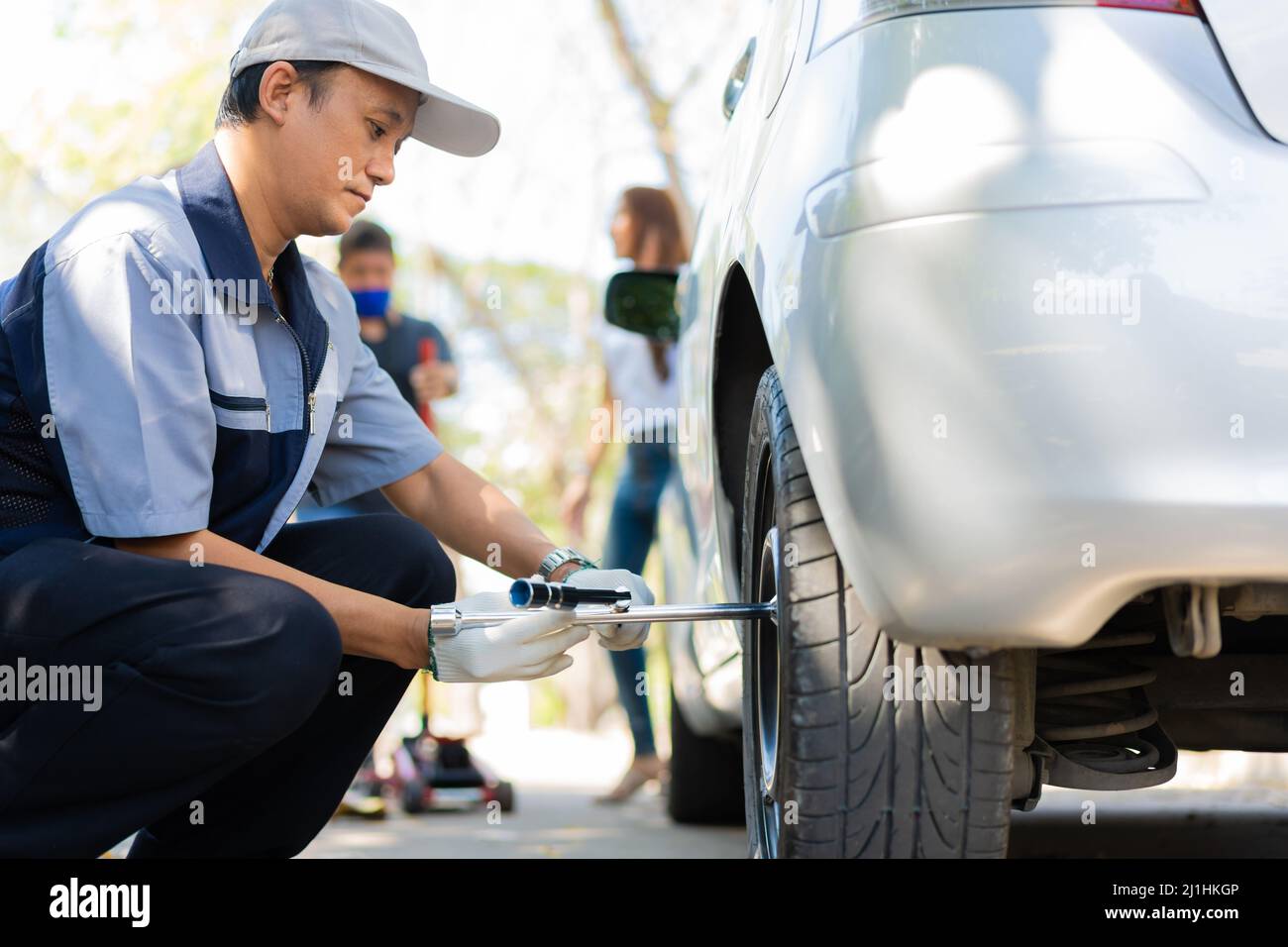 Expertise mechanic man  in uniform using force trying to unscrew the wheel bolts nuts and help a woman for changing car wheel on the highway, car serv Stock Photo