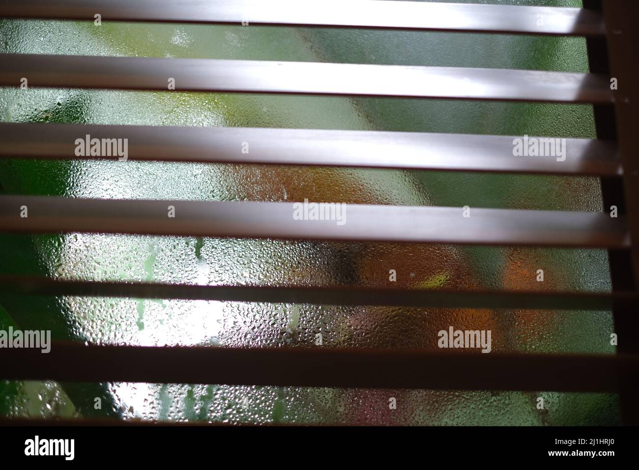 Half-closed wooden blinds with colorful fogged up window behind Stock Photo