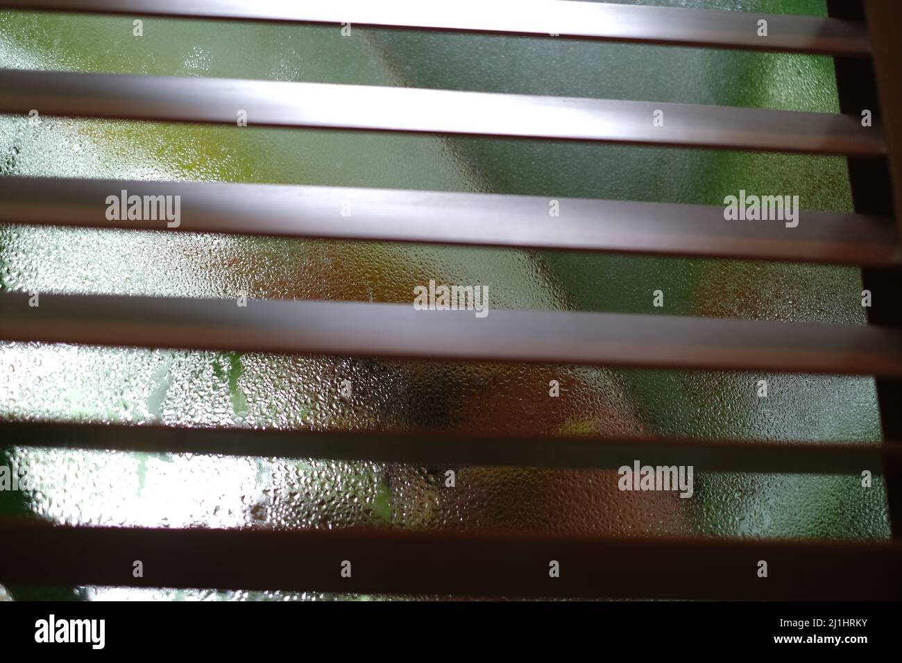 Half-closed wooden blinds with colorful fogged up window behind Stock Photo
