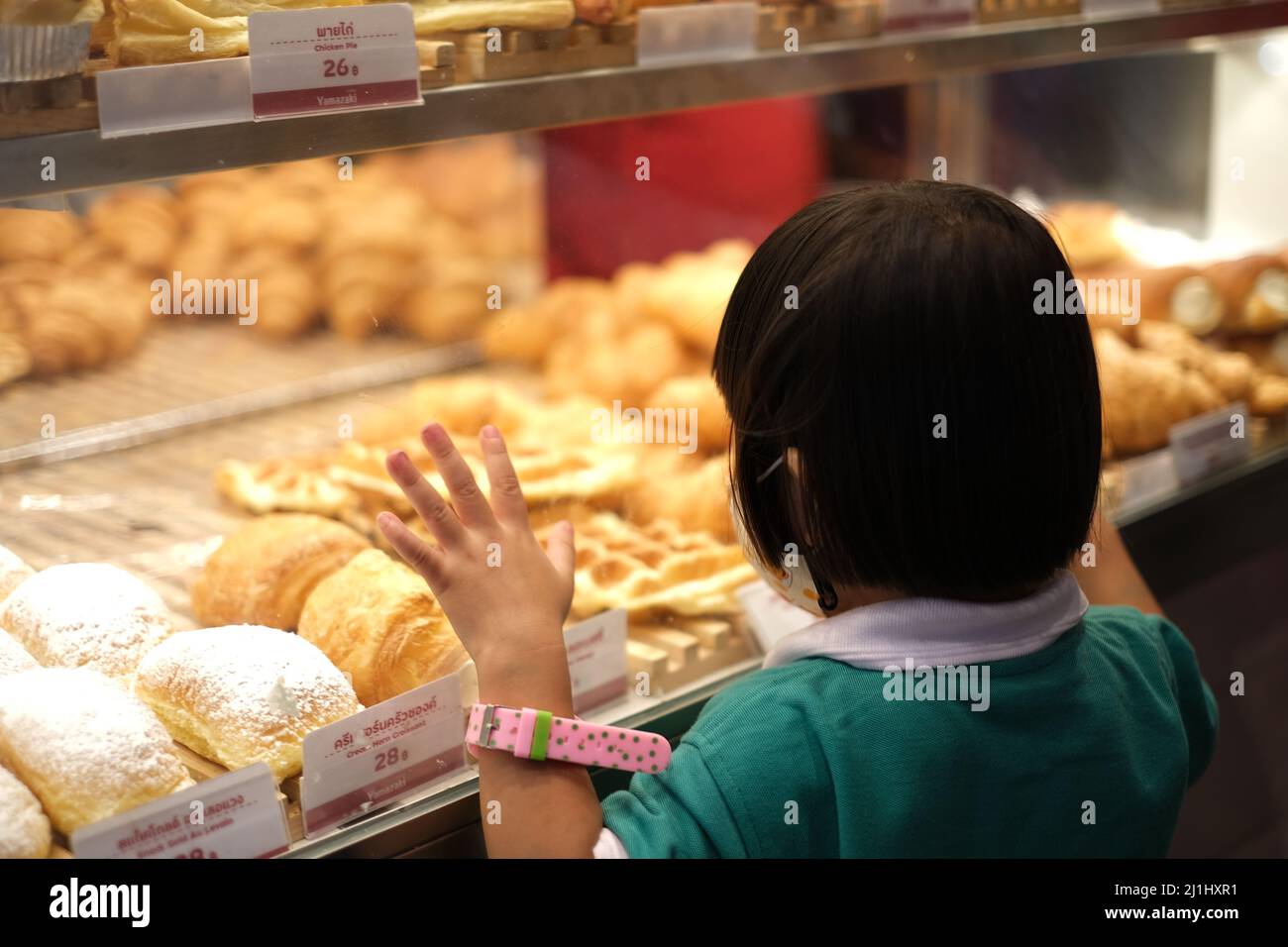 Young girl clings to bakery showcase at Thai night market, looking thirstily to numerous buns, pies and muffins Stock Photo