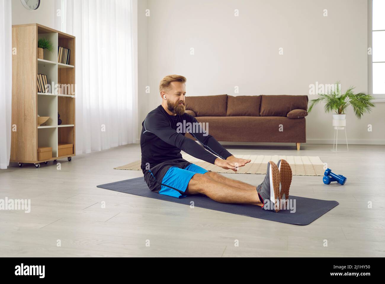 Athletic man at home doing sports stretching stretching his arms to tips of his legs. Stock Photo