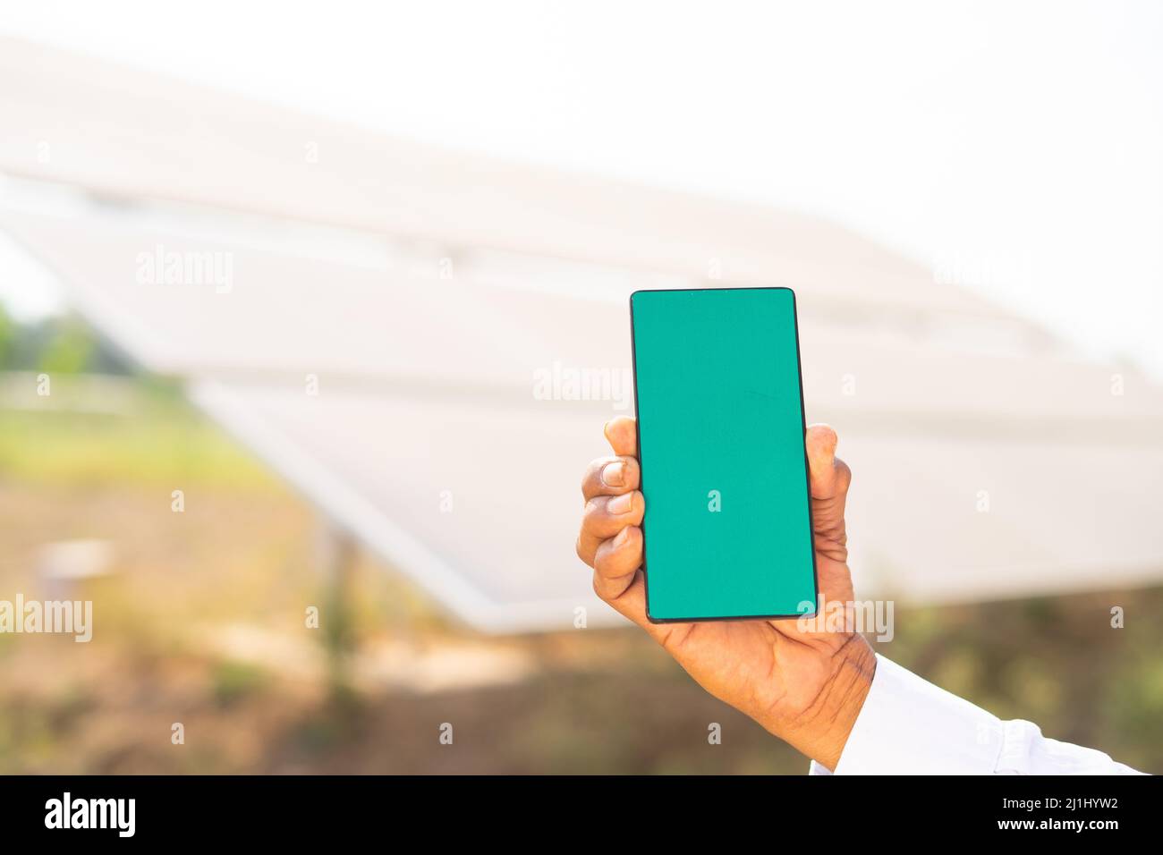 close up of farmer hands showing green screen mobile phone while standing in front of solar panel at farmland - concept of app advertisement Stock Photo