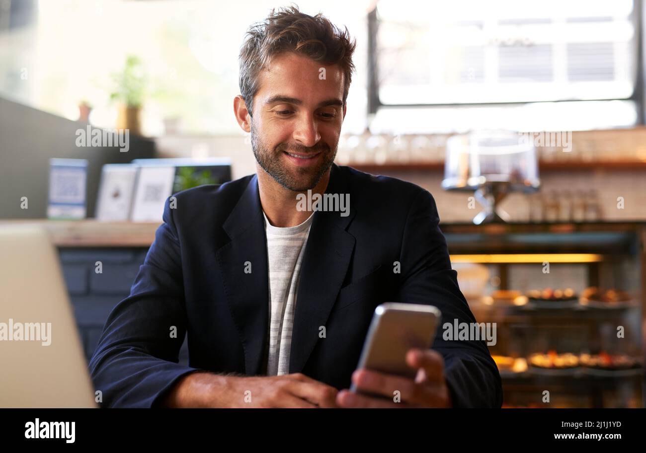 He knows how to get things done. Shot of a handsome young man using a phone and laptop in a cafe. Stock Photo