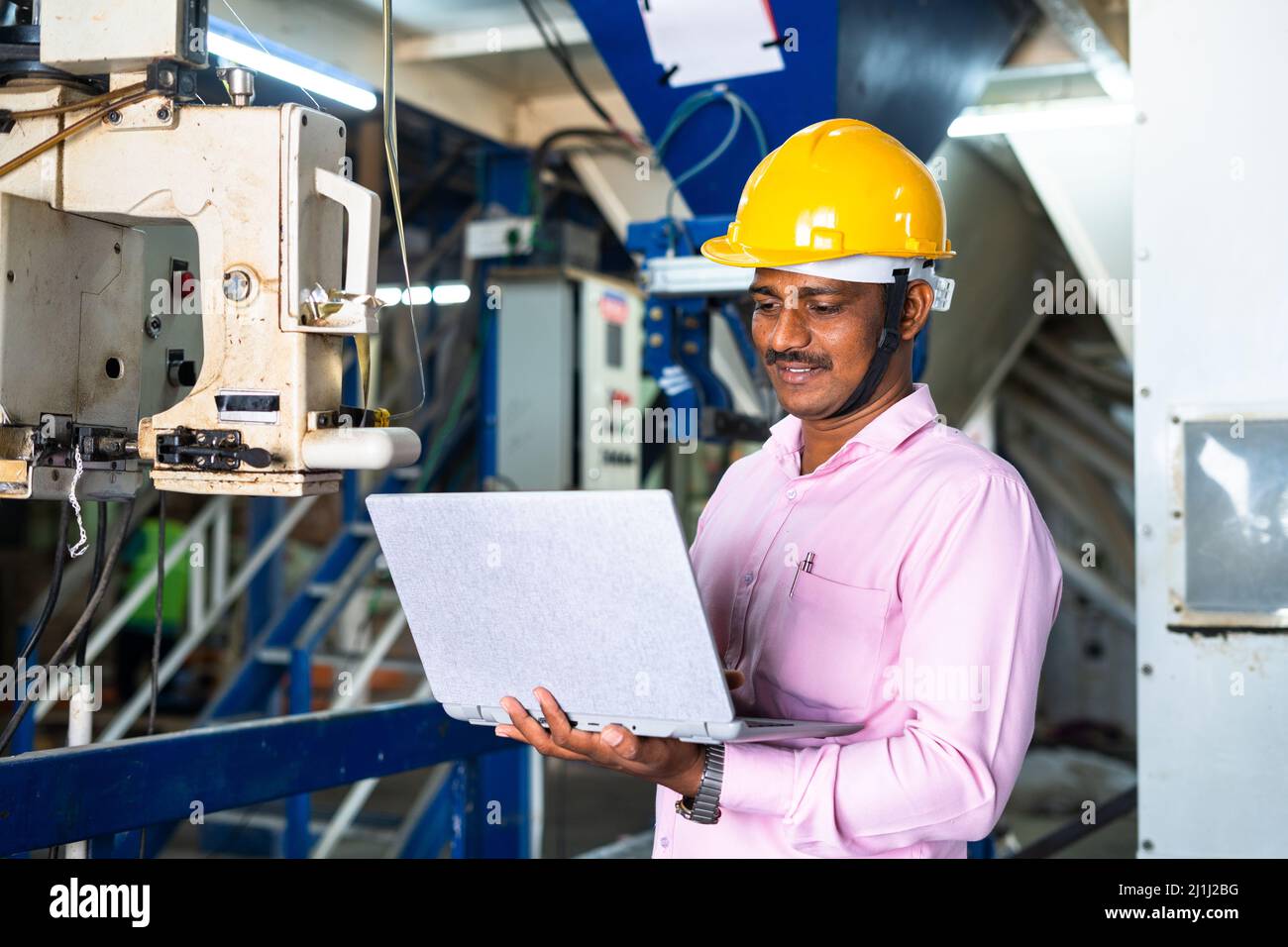 engineer in uniform busy working on laptop at machinery in factory - concept of technology, skilled or professional labour and development. Stock Photo