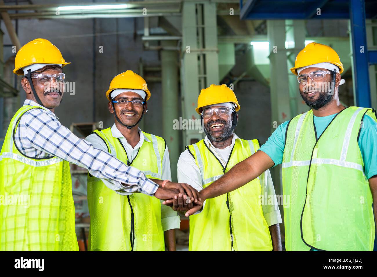 factory workes witj safety hard hat joining hands at workplace - concept of teamwork, cooperation and partnership Stock Photo