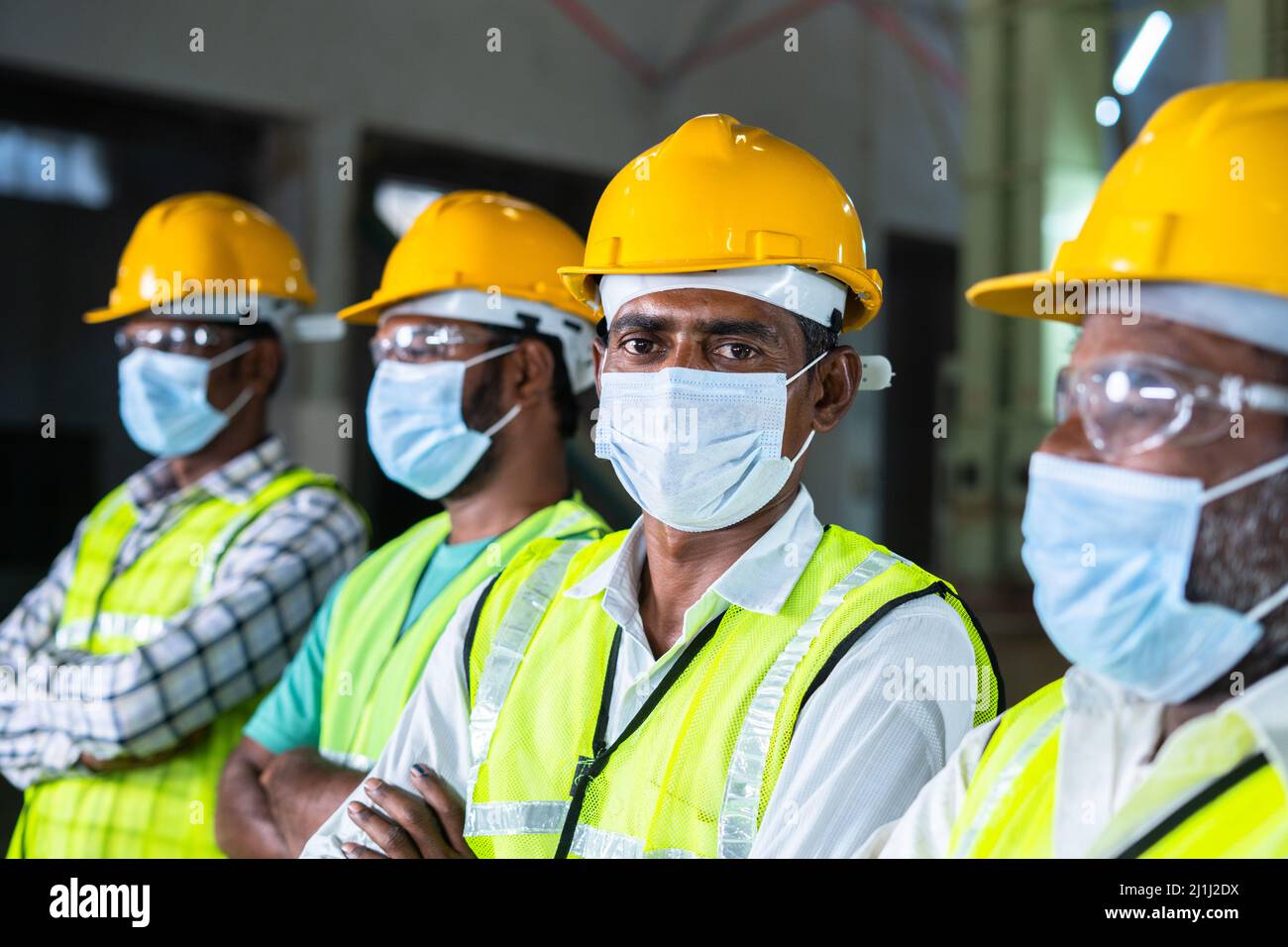 group of factory workers with face mask, eyeglasses and hardhat looking at camera by - concept of industrial safety measures and protection from Stock Photo