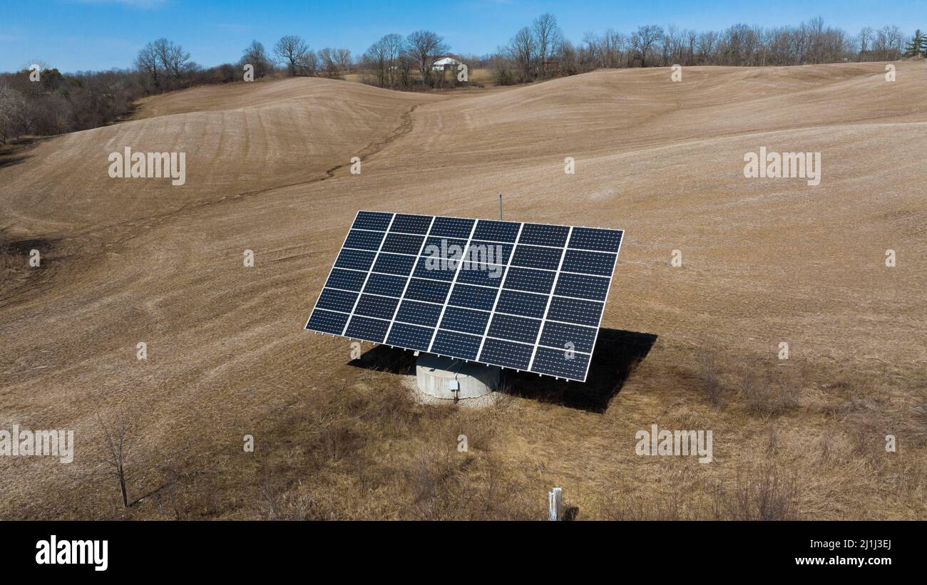 A low aerial view of a large solar tracker in a rural field is seen on a clear, sunny day. Stock Photo