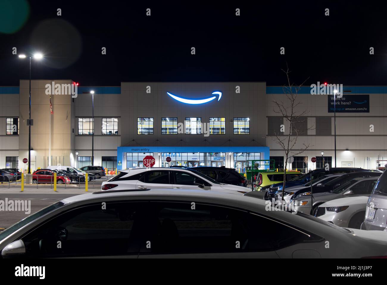 The Amazon logo shines brightly in blue at the top of the front entrance to a large, new fulfillment center near an airport. Stock Photo