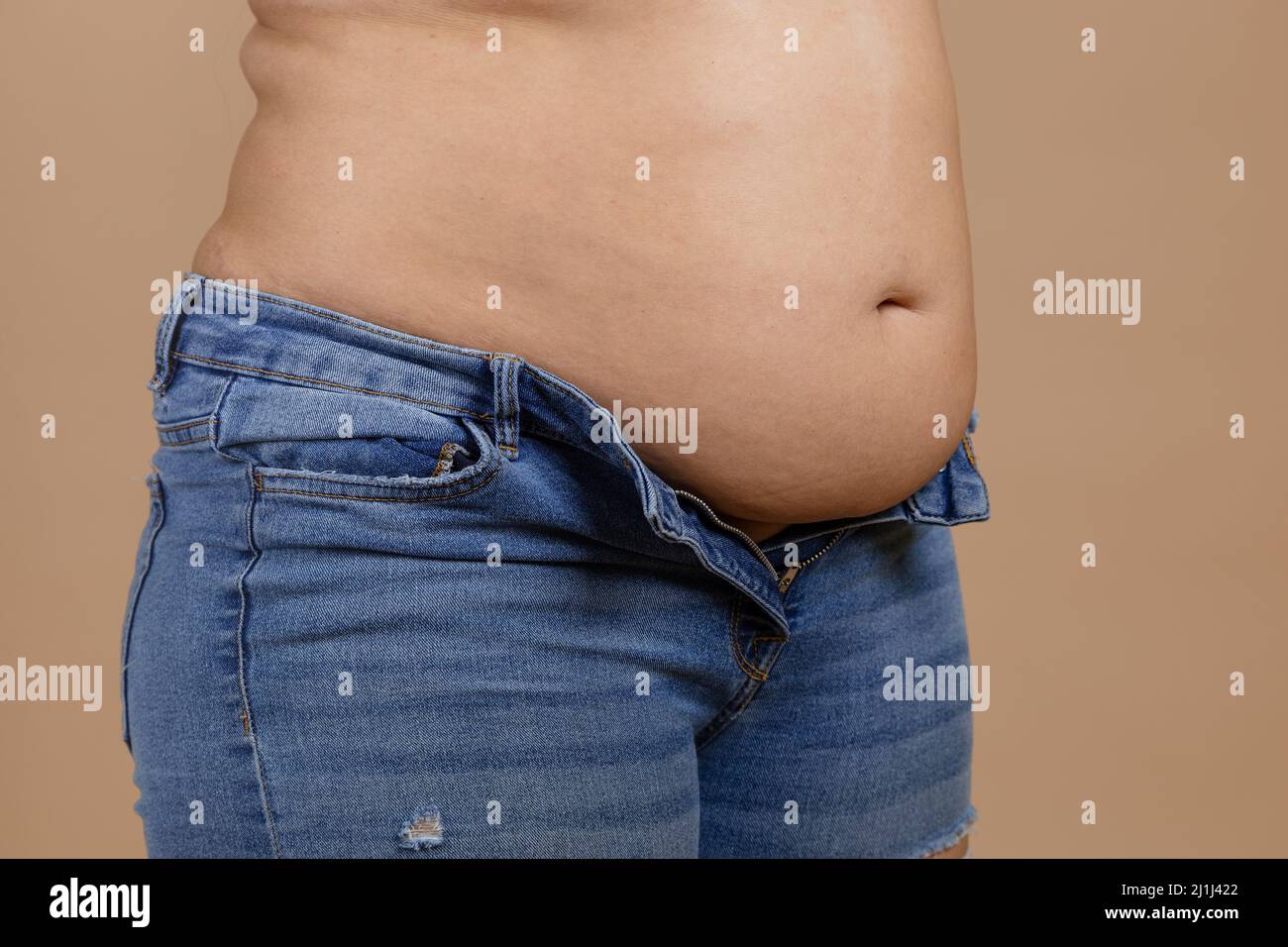 Overweighted plumpy lady with flabby stomach and fat sides showing waist in unzipped jeans. Sudden weight gain. Visceral fat. Body positive. Tight Stock Photo