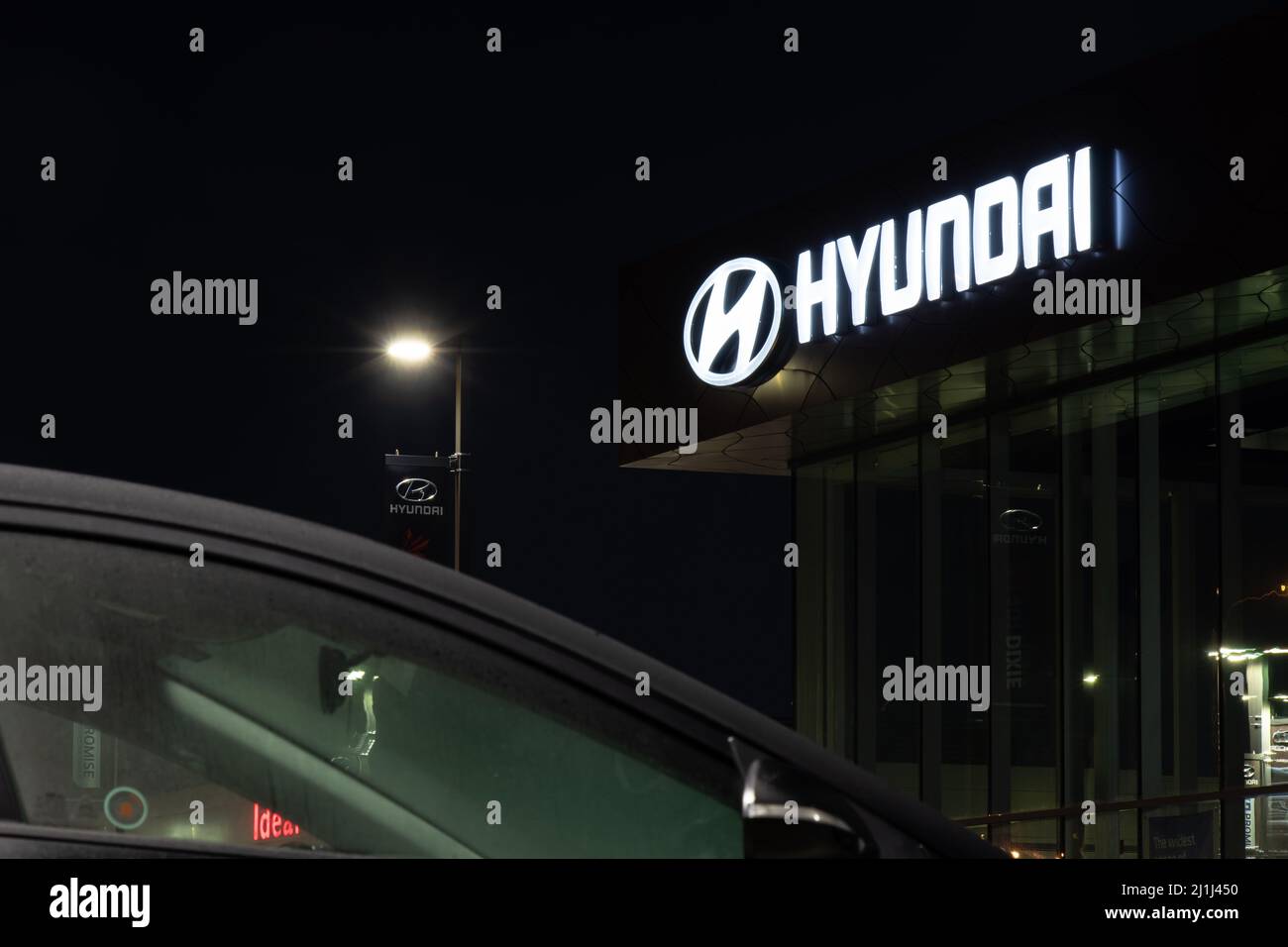 A Hyundai sign glows brightly at night atop a Hyundai car dealership. Stock Photo