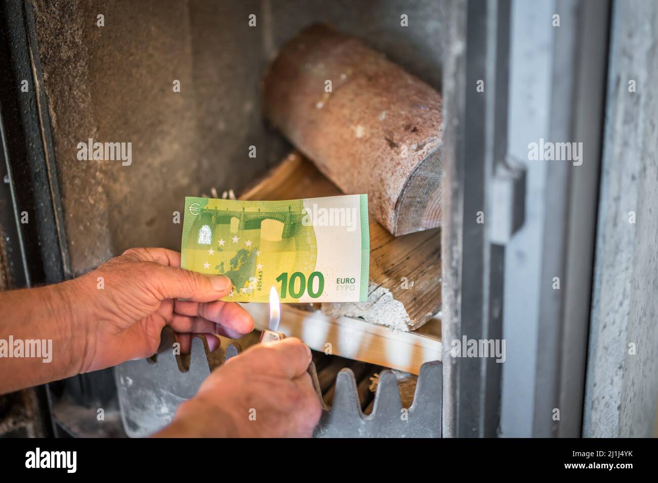 Old pensioner man holding banknotes in hand in front of wood stove with wood and burning lighter in an apartment, Germany Stock Photo