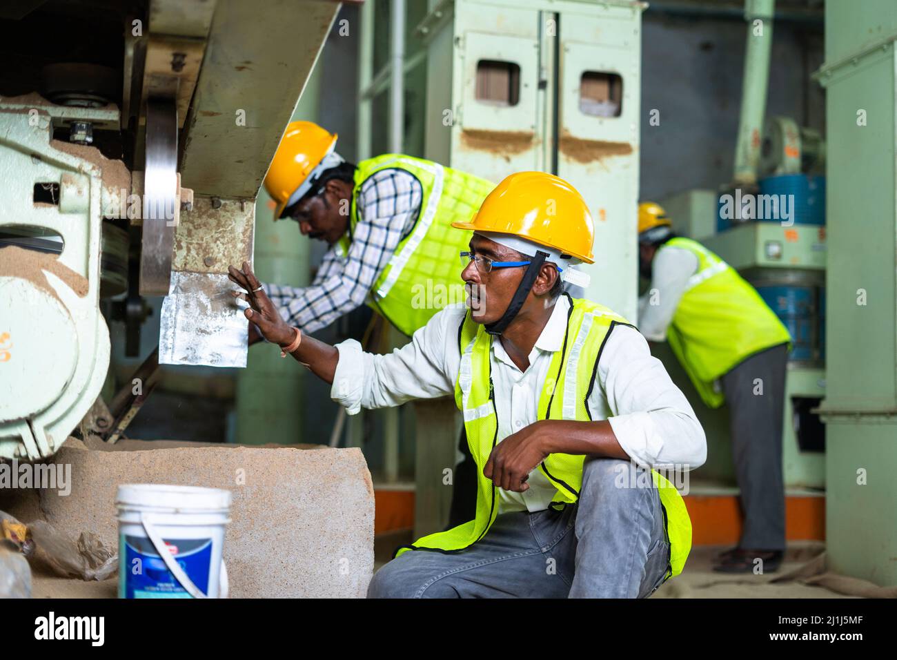 Industrial workers busy working on machinery with safety helmet at factory - concept of blue collar jobs, teamwork and occupation Stock Photo