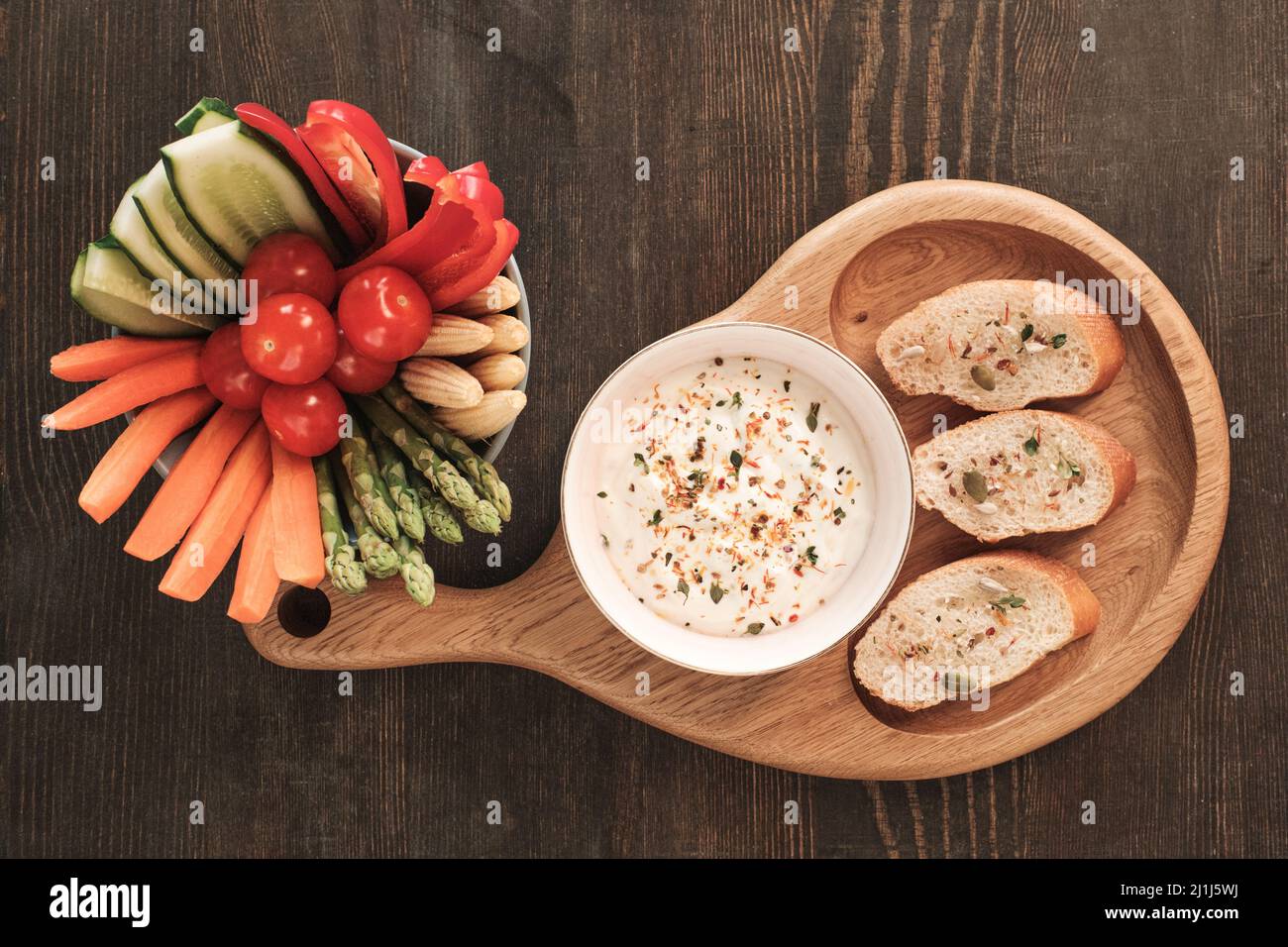 Directly above view of healthy vegetable snacks and baguette slices with white sauce on wooden dining table Stock Photo
