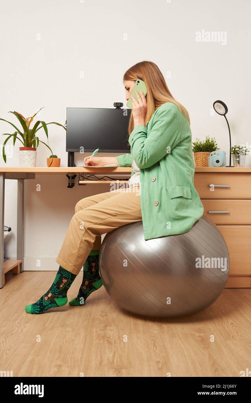 Woman working from home uses fitness ball as a chair Stock Photo