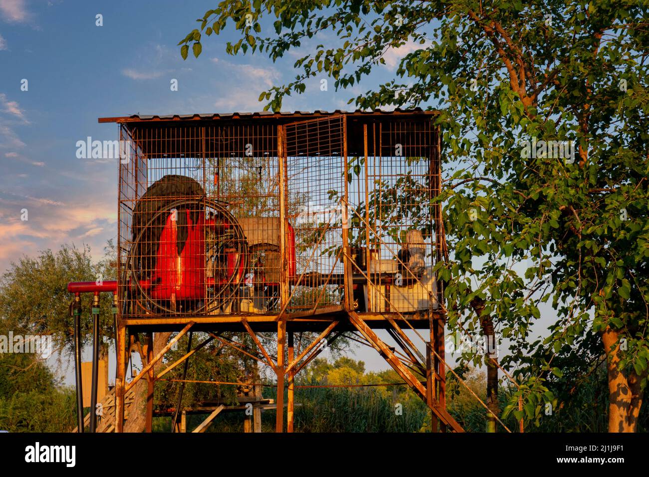 Water motor in cage used for drip irrigation. red watering engine. Sunset. Stock Photo