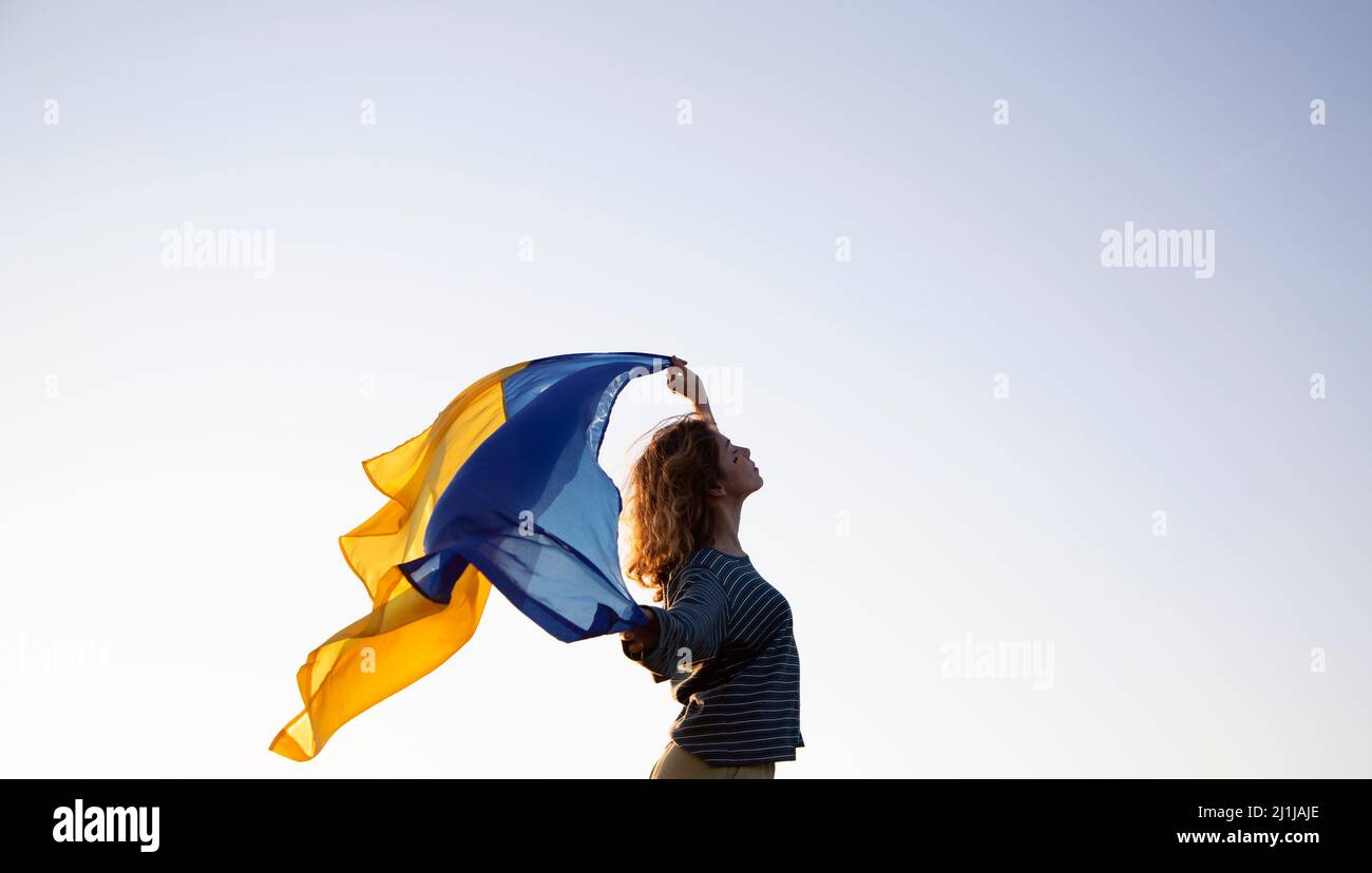 sunset, a woman's silhouette holds behind her back the Ukrainian flag fluttering in the wind. Ukrainians against the war. Drawing attention to militar Stock Photo