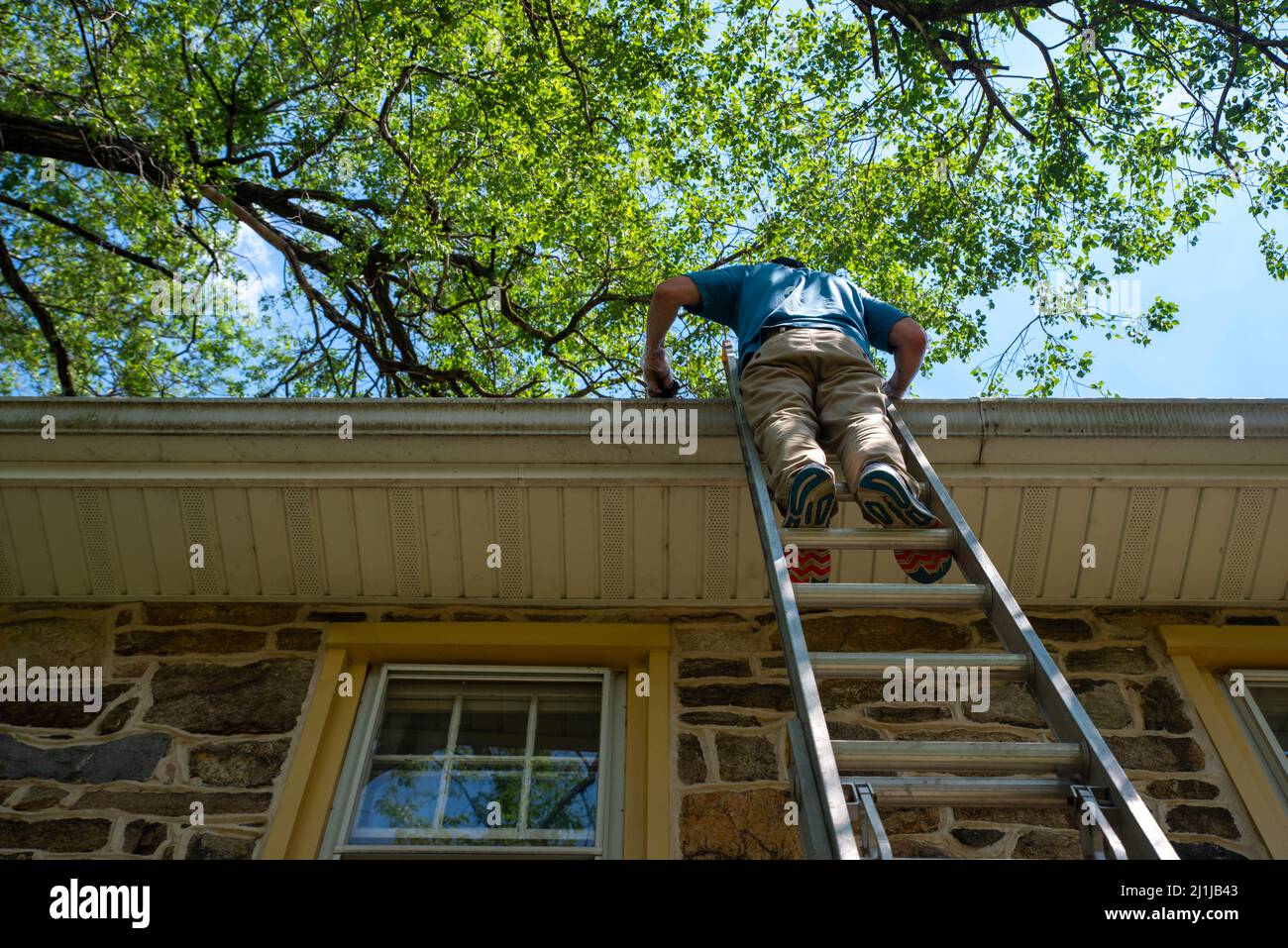 Low angle view of off center man on ladder cleaning gutters of a stone ...