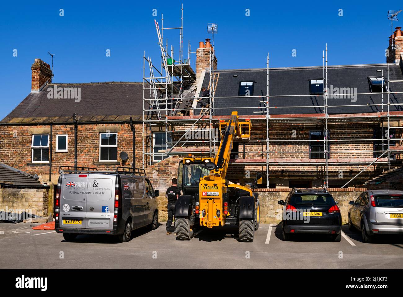 Modernising, refurbishing row of houses (roofer on ladder, man in yellow JCB operator cab, scaffolding) - Knaresborough, North Yorkshire, England, UK. Stock Photo
