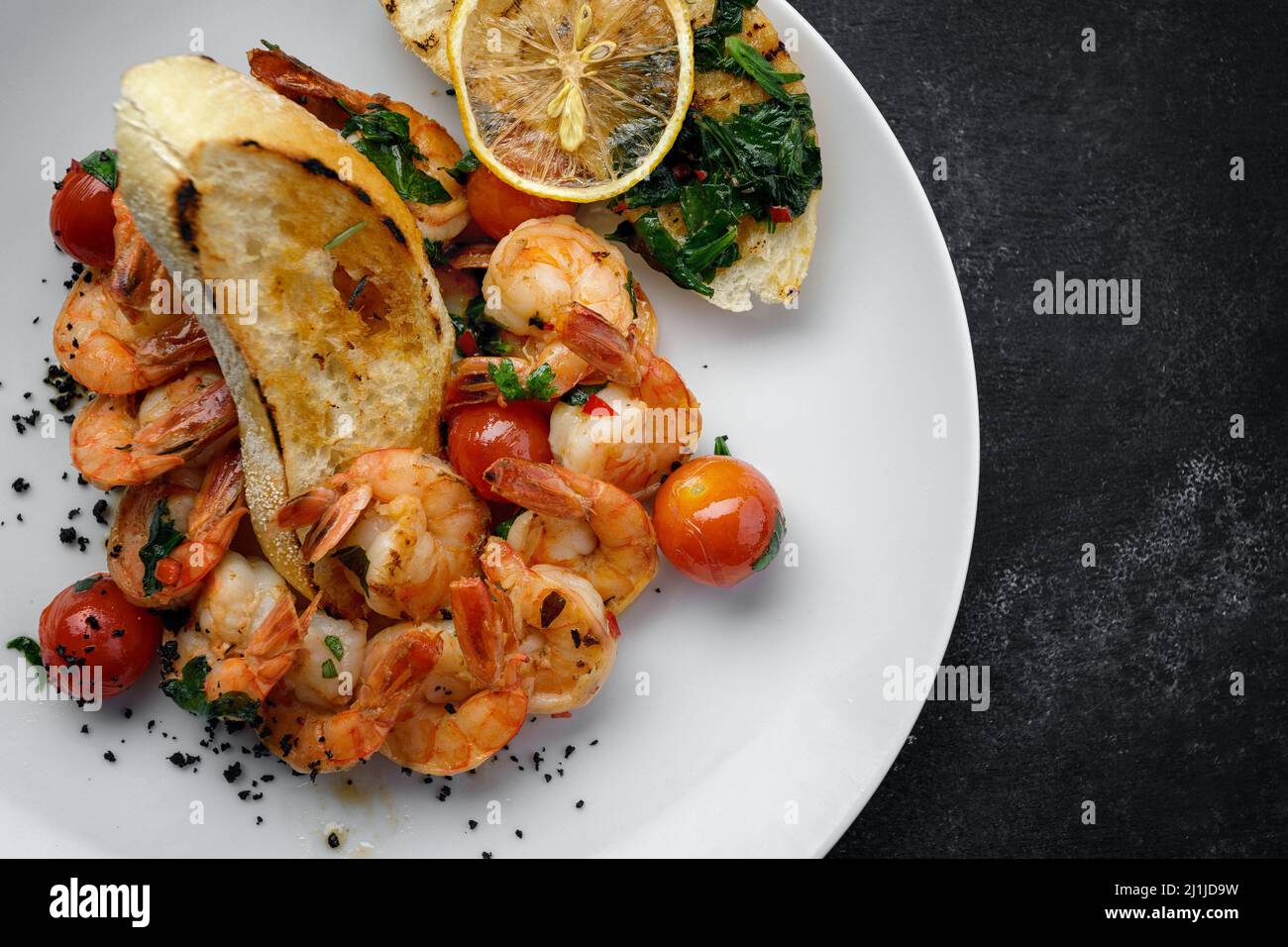 Fried shrimp in tomato sauce with lemon and tomatoes, on a plate with