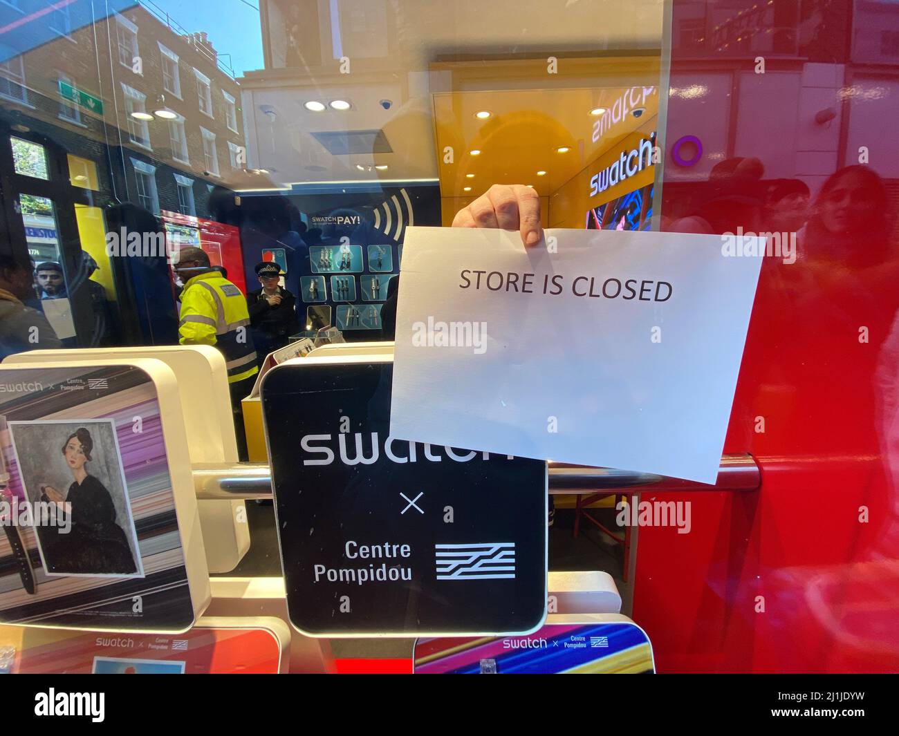 A retail assistant puts a 'Store is Closed' sign in the window of the Swatch store on Carnaby Street, central London, after chaos broke out at the launch of the MoonSwatch, with late customers trying to barge their way into the store ahead of those who had waited in line overnight. The Omega x Swatch collaboration is a collection of solar system-inspired watches based on Omega's Moonwatch, the first wristwatch worn on the moon, but available for a fraction of the price. Picture date: Saturday March 26, 2022. Stock Photo