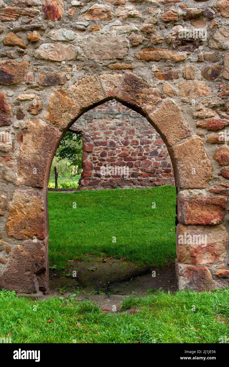 Passage through an old sandstone wall in the form of a pointed arch in a ruined monastery with deep green grass on the ground Stock Photo