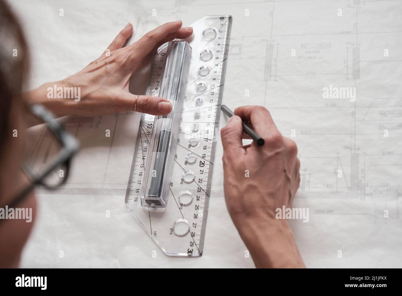 Over shoulder view of female architect or engineer drawing blueprint using ruler and pencil Stock Photo