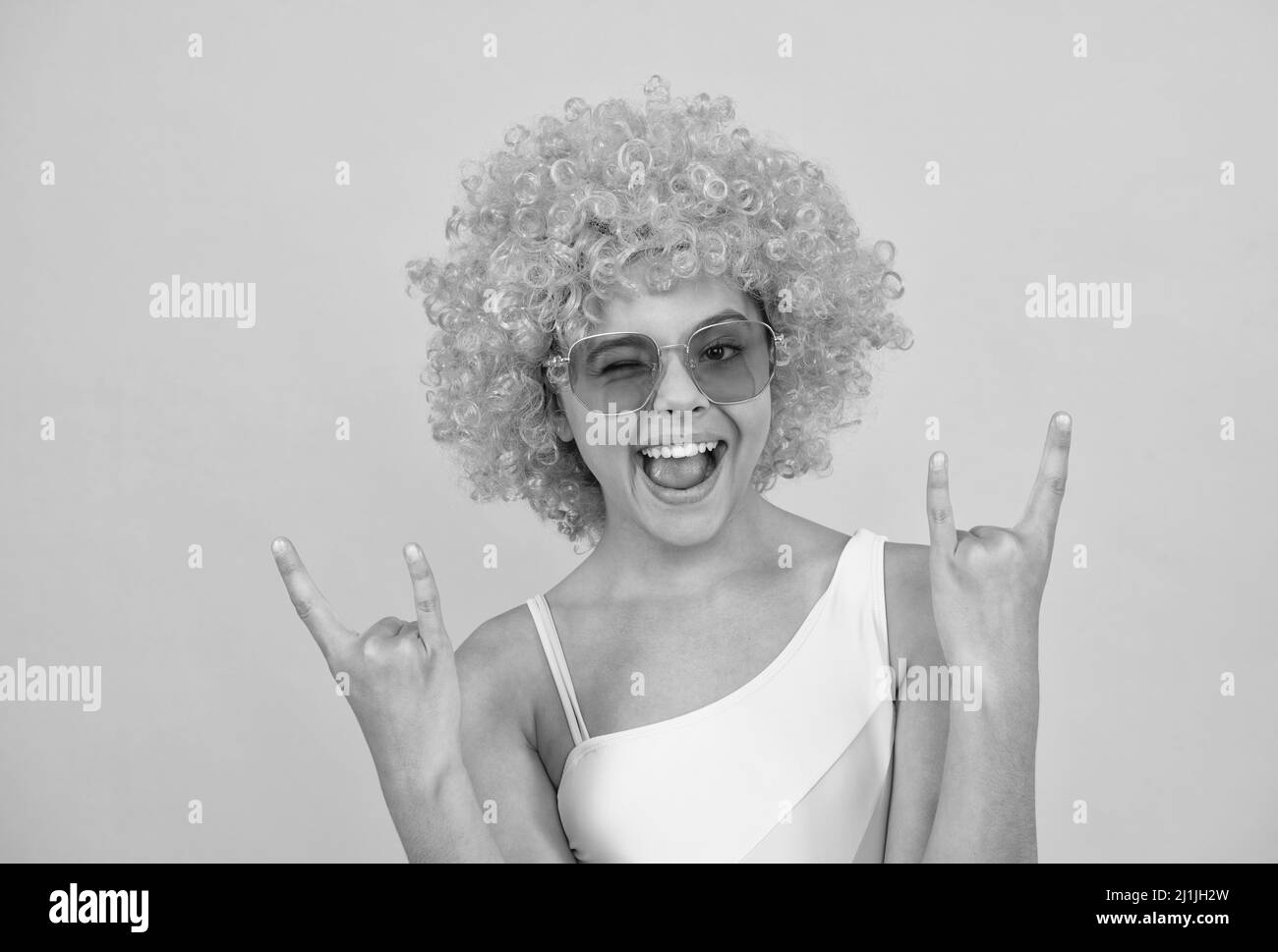 happy cool teen girl in sunglasses wearing orange curly wig hair on yellow background, childhood. Stock Photo
