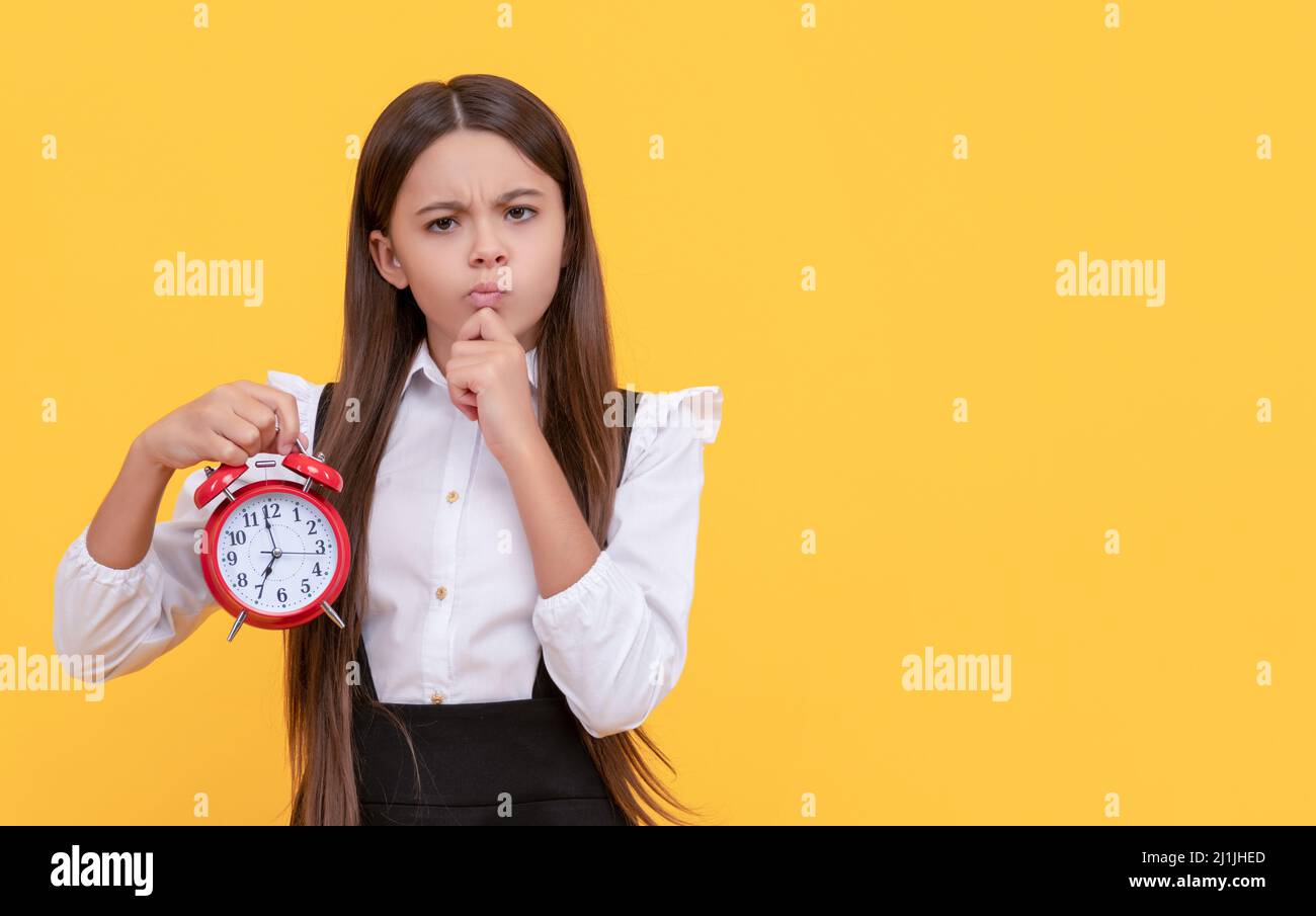 pondering child with alarm clock. school kid in uniform showing time