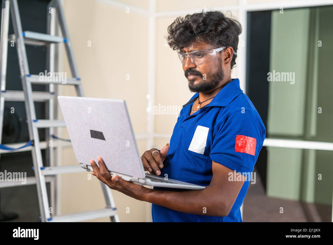 Aluminium partition worker busy using laptop at construction site - concept of technology, renovation and maintenance service. Stock Photo