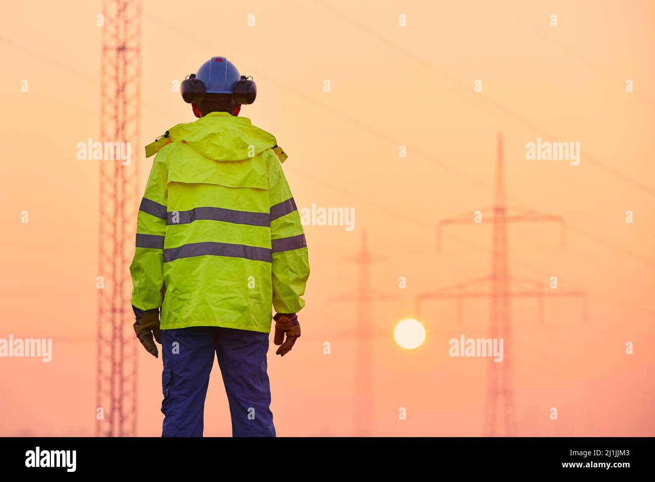 Rear view of electrical engineer against electricity pylons during frosty winter morning. Themes energy supply, industry and environment. Stock Photo