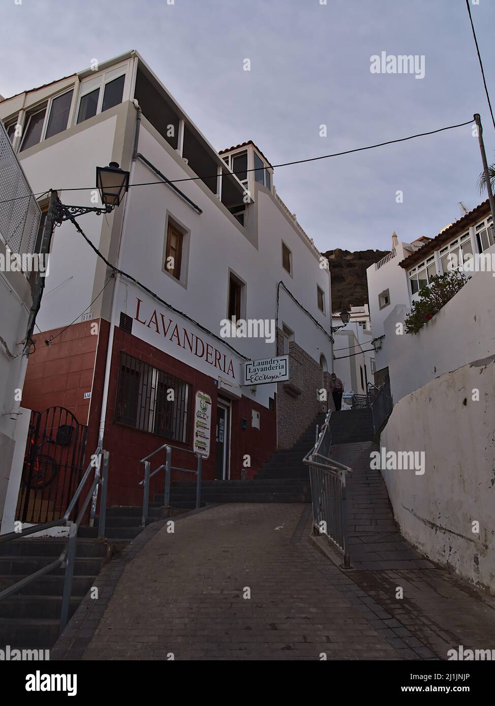 Beautiful view of a narrow alley in the old town of Puerto de Mogan, Gran Canaria, Spain in the evening with laundry shop and cloudy sky. Stock Photo