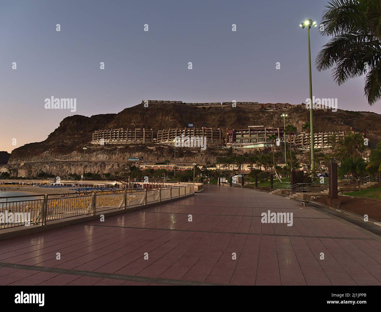 View of empty promenade at popular beach Playa de Amadores near Puerto Rico, southern Gran Canaria, in the evening with hotel buildings on the slope. Stock Photo