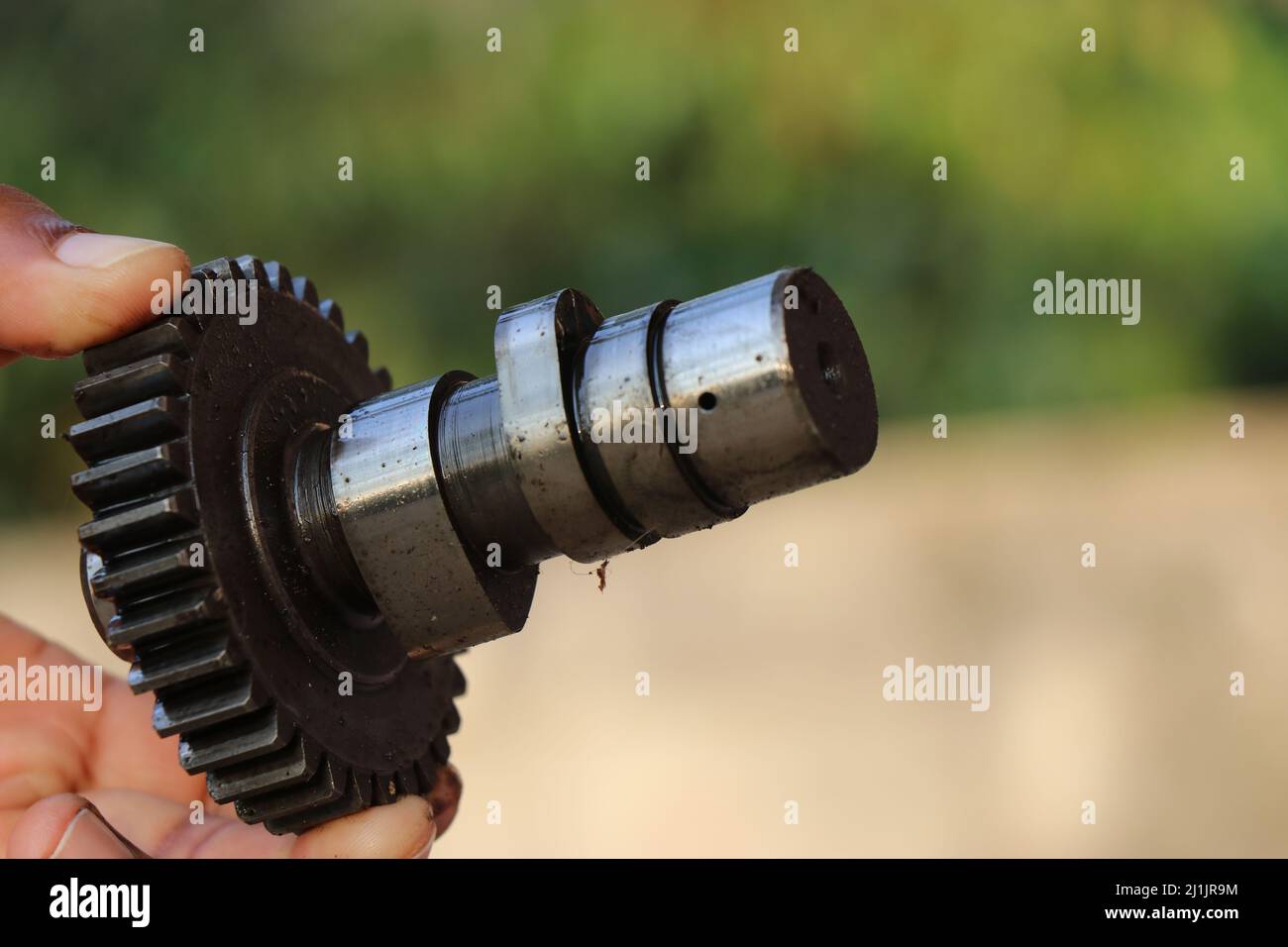 Camshaft with gears held in hand isolated on nature background