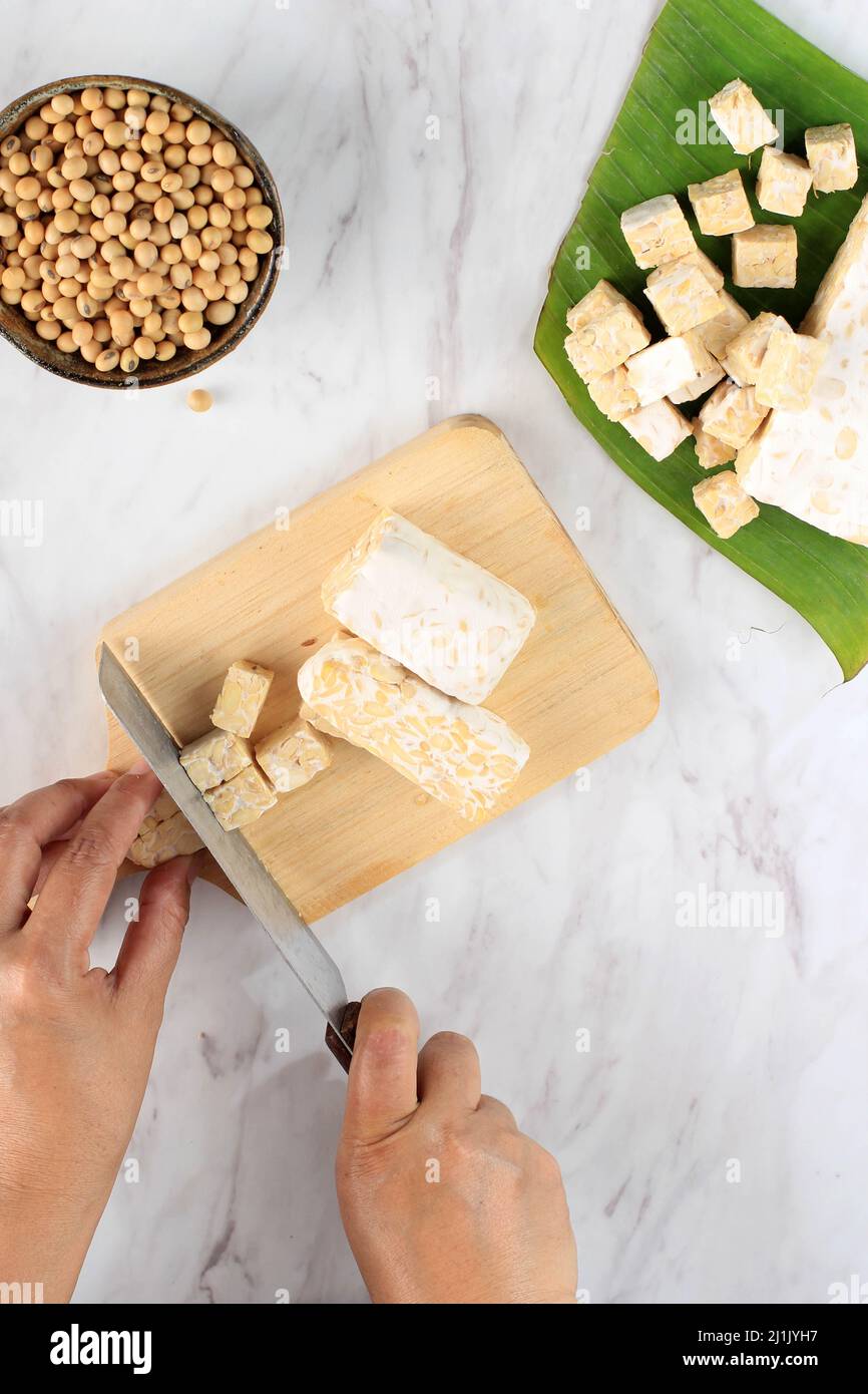 Selected Focus Female Hand Slicing Cut Tempeh or Tempe on Wooden