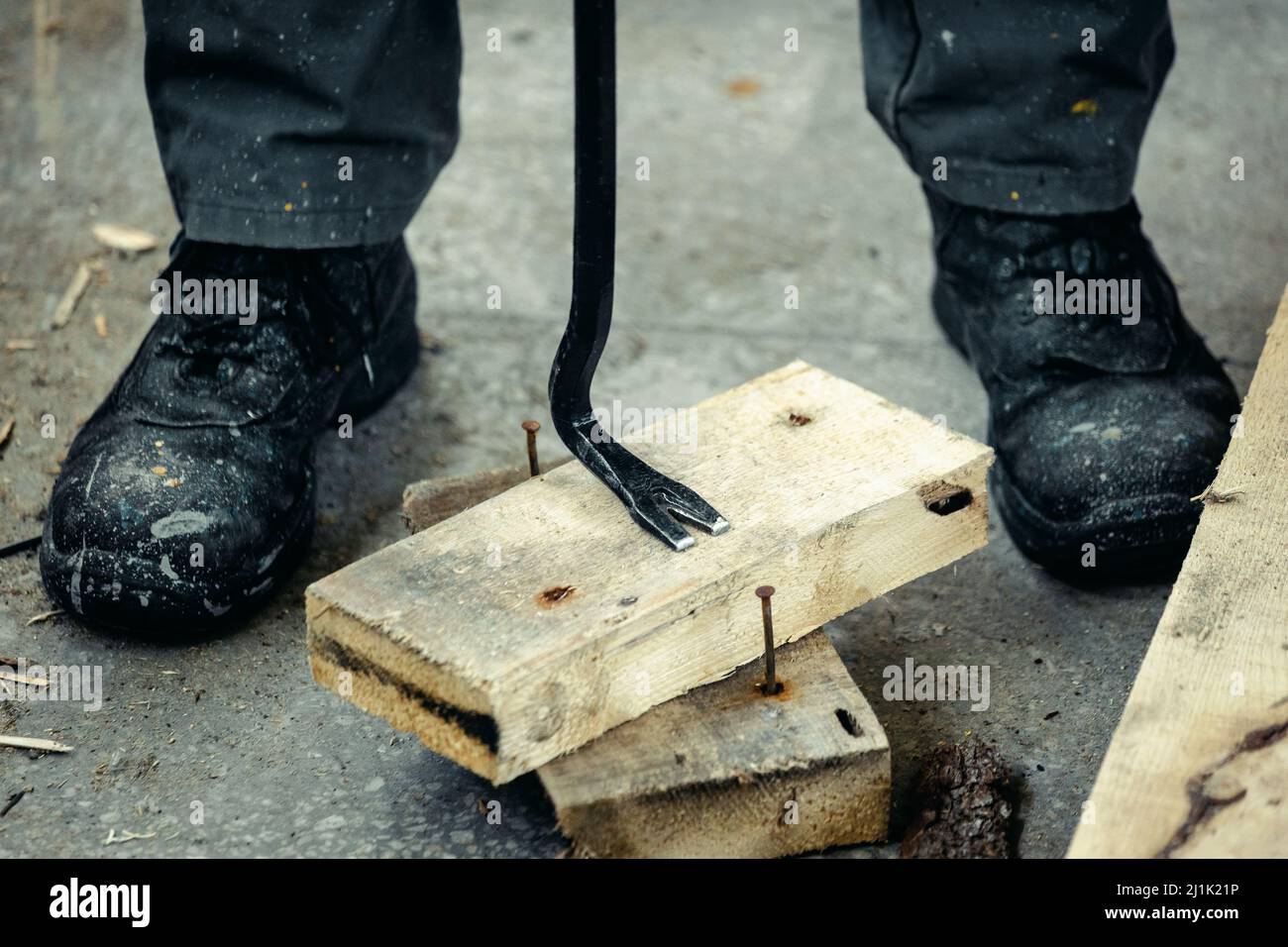 Worker in rough boots pulls nails out of wooden planks. Construction and repair. Background. Stock Photo