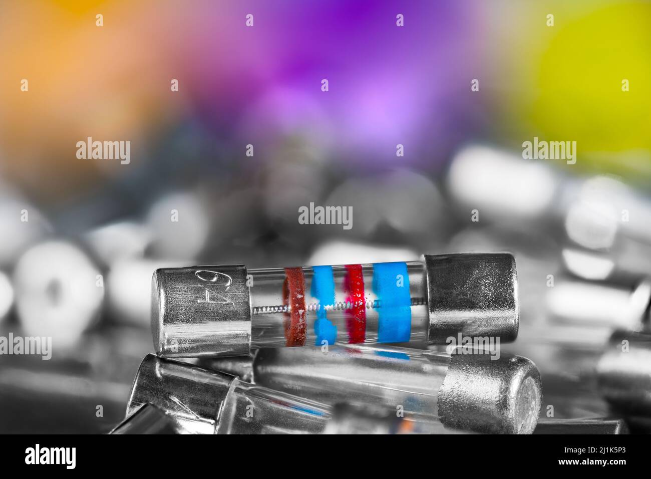 Closeup of small electrical fuses pile on a blurry background with colored and white bokeh. Safety device for overcurrent protection with fusible wire. Stock Photo