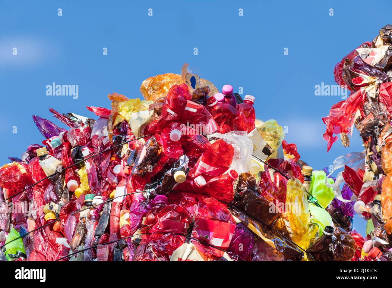 Detail of red plastic waste compressed in bale on trash landfill with blue sky background. Close-up of used crumpled PET bottles on dump. Eco problem. Stock Photo