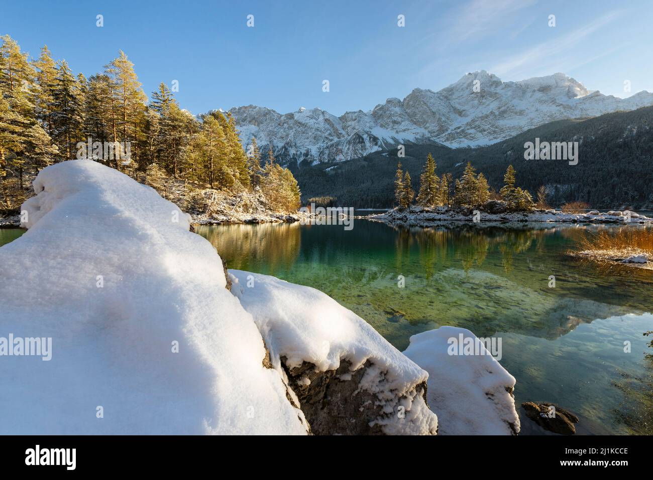 Snow-covered mountain forests and the Wetterstein range with Zugspitze in the afternoon sun reflected in the turquoise water of Lake Eibsee, Bavaria Stock Photo