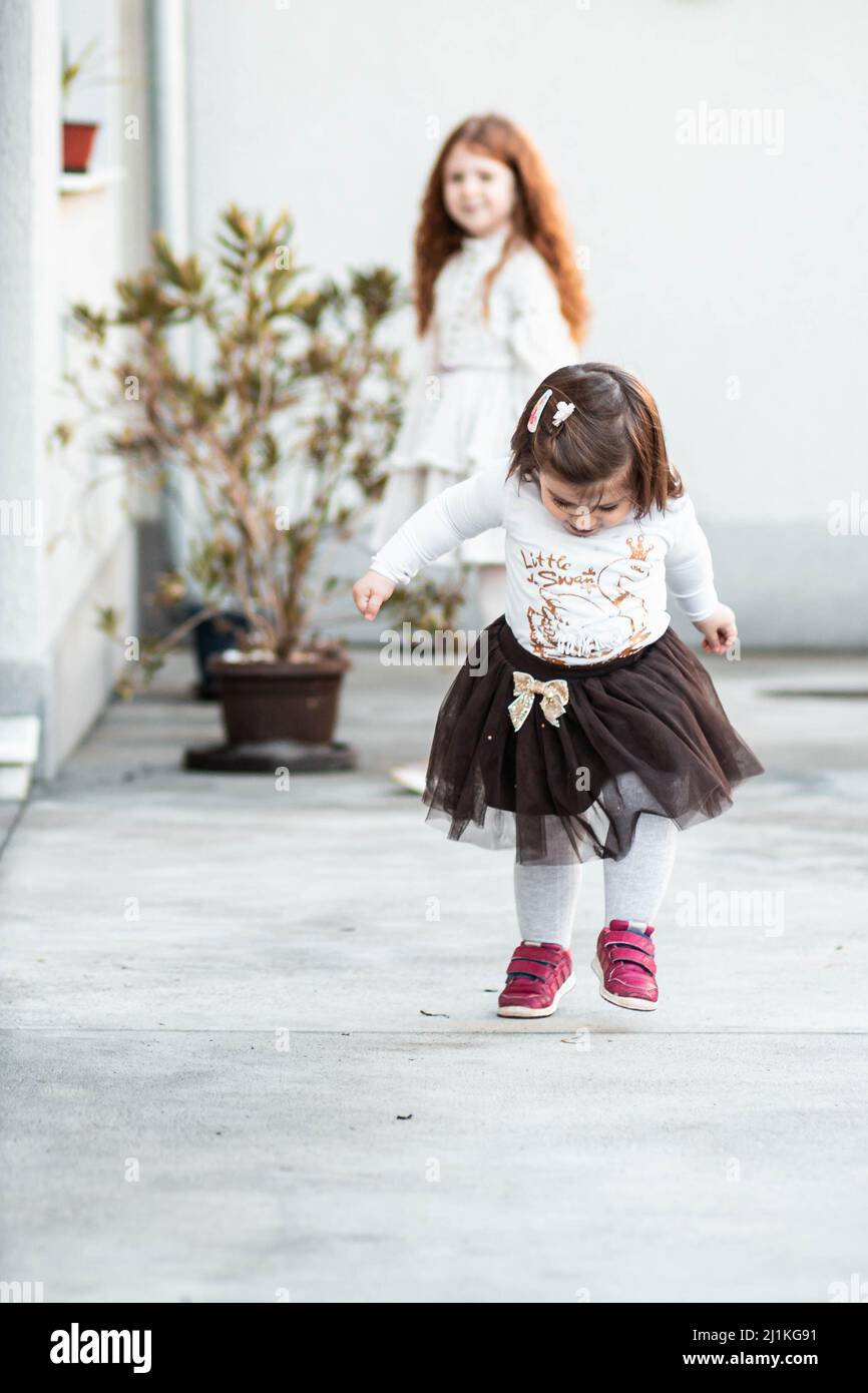 Cute, little toddler girl walking outdoors with her sister watching in the background Stock Photo