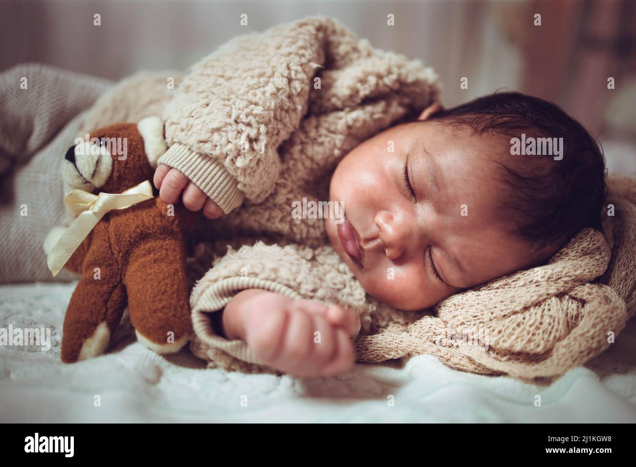 Infant multiethnic baby boy sleeping on a bed. Looking cozy with teddy bear Stock Photo