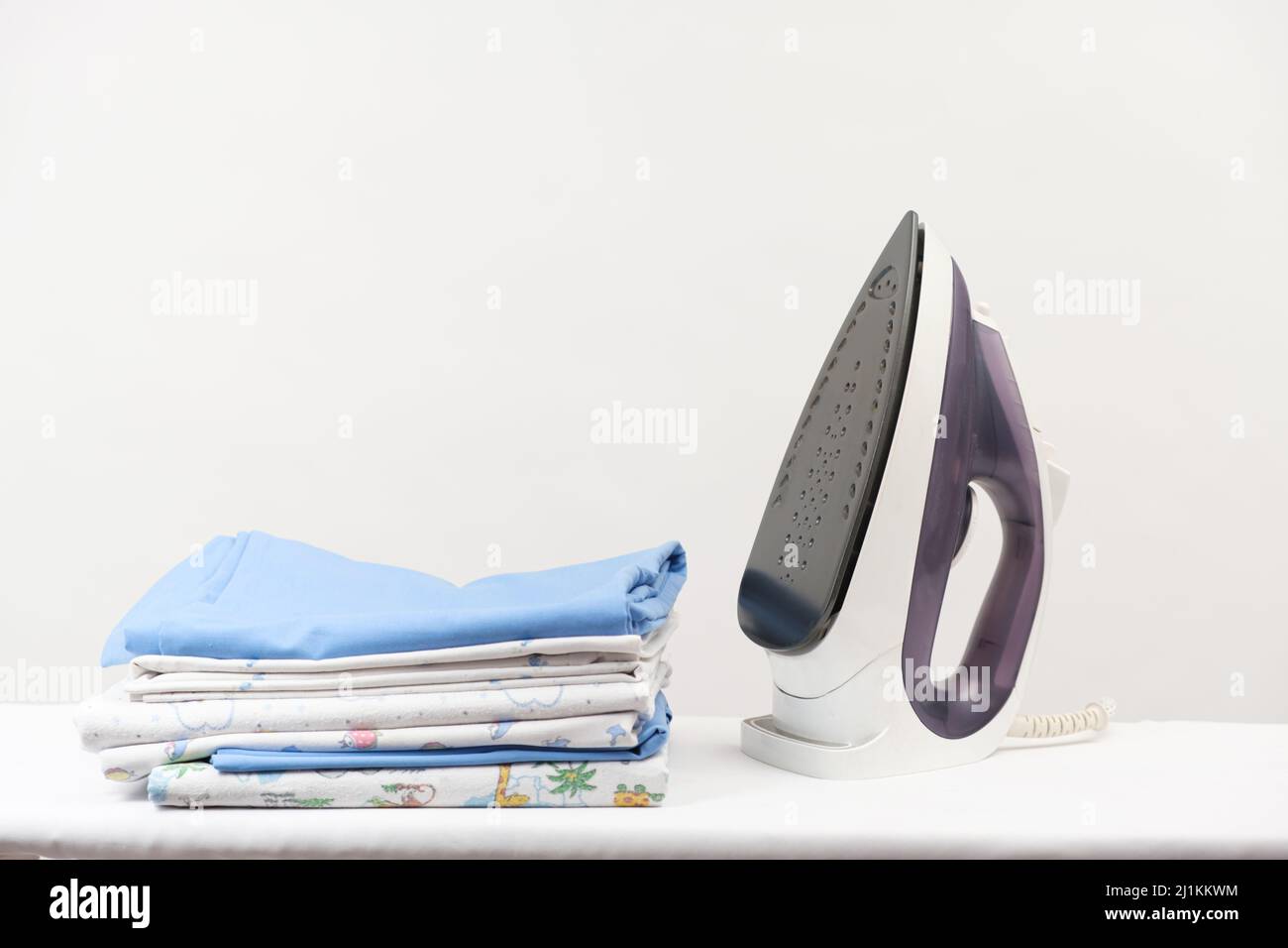 Iron and a stack of ironed clothes and baby diapers on a white background with space for text. Stock Photo