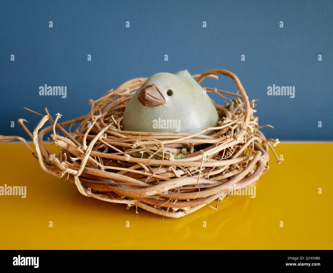 Ceramic Easter hen in willow nest on yellow sideboard against blue wall