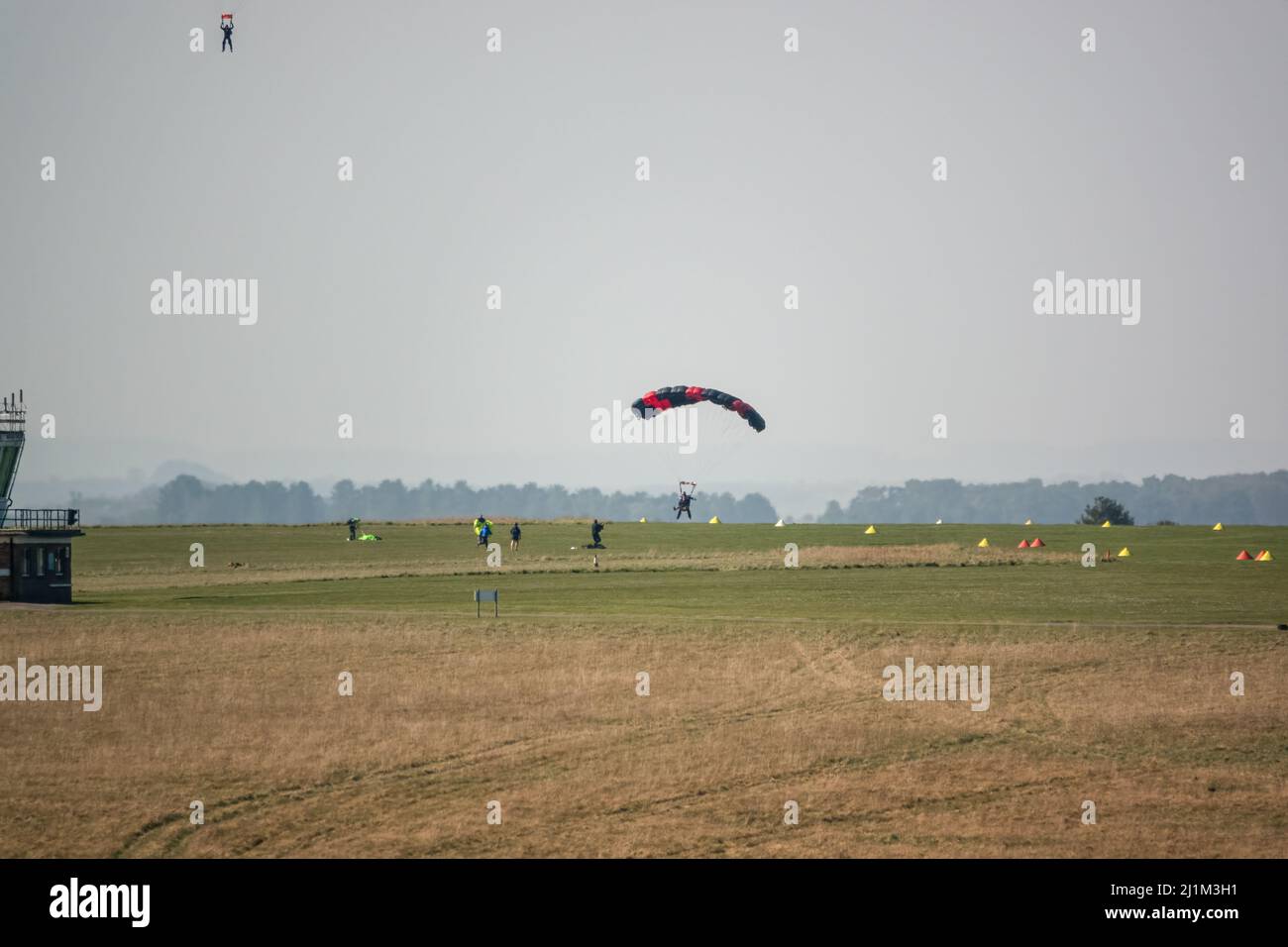 Parachute jumper coming in to land on a grass airfield, blue sky Stock Photo