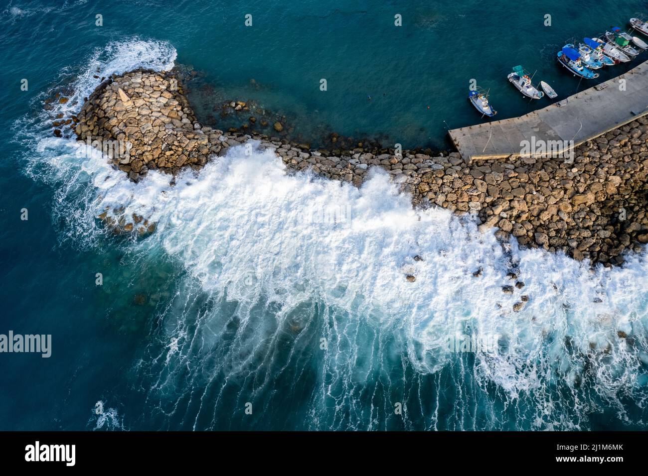 Aerial drone view of fishing boats moored at the harbor at breakwater. Stormy waves at sea Stock Photo