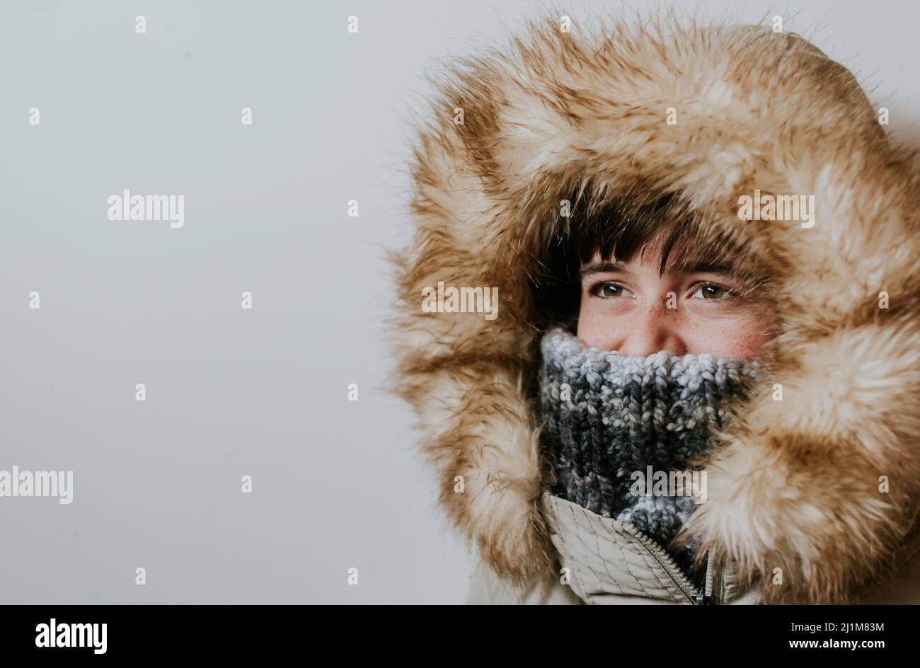 Boy wearing winter coat with furry hood against white background. Stock Photo