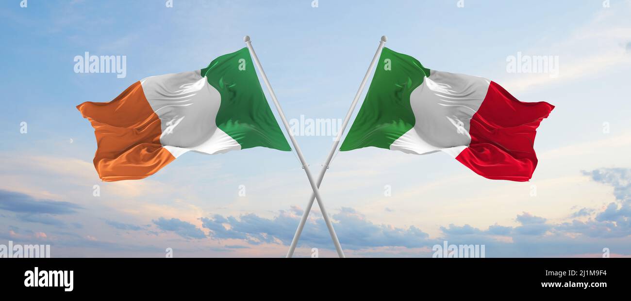 two crossed flags Ireland and Italy waving in wind at cloudy sky ...