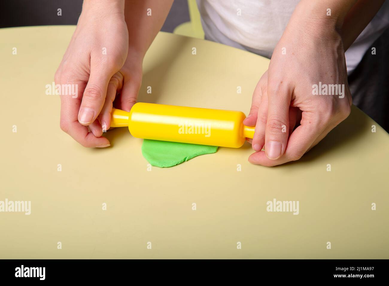 A child and his mother roll out a piece of green dough on the table with a rolling pin, close-up of hands Stock Photo