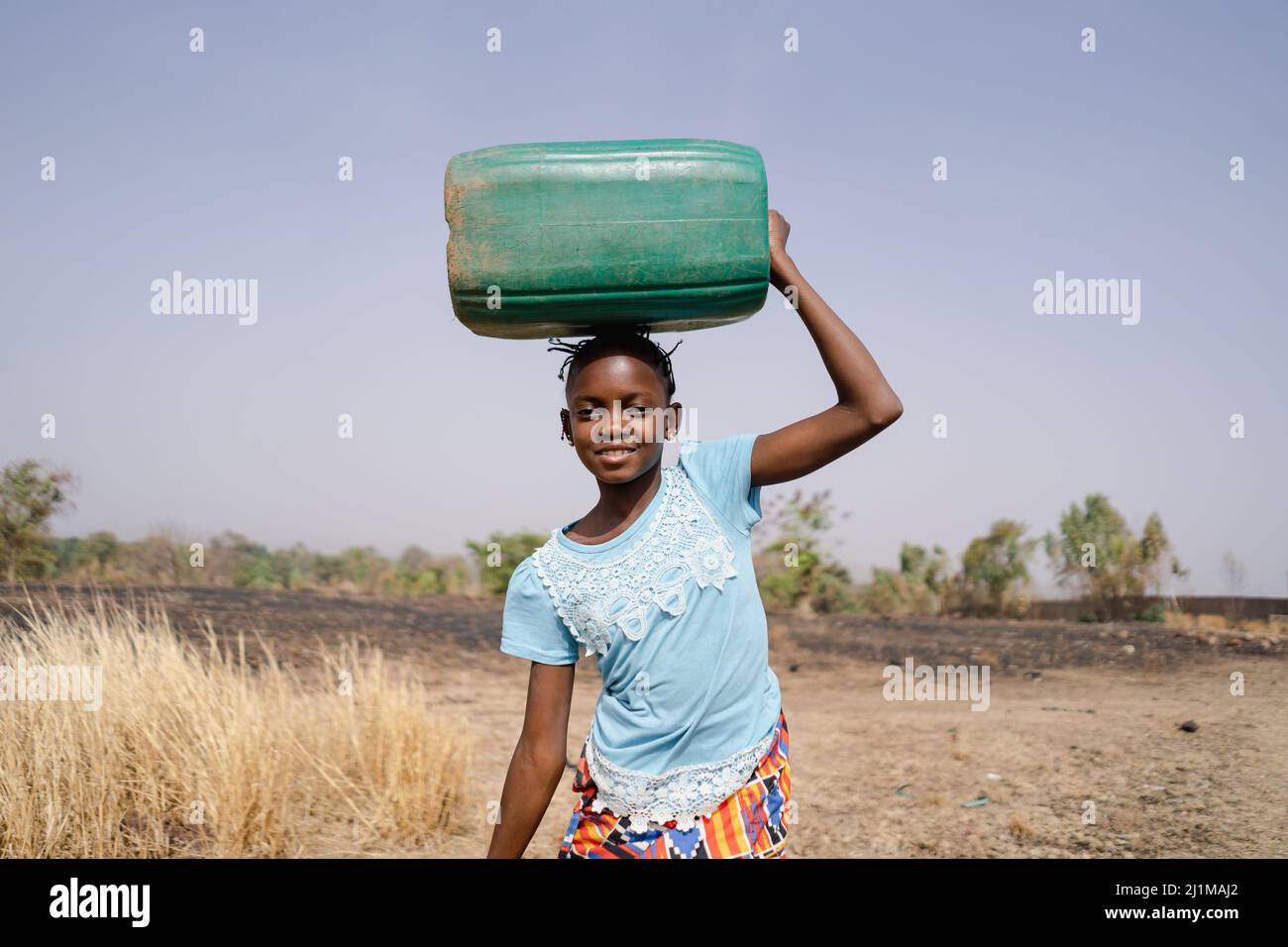 Brave young African girl on her long and arduous walk home from the distant village well, wasting hours of time instead of going to school; social iss Stock Photo